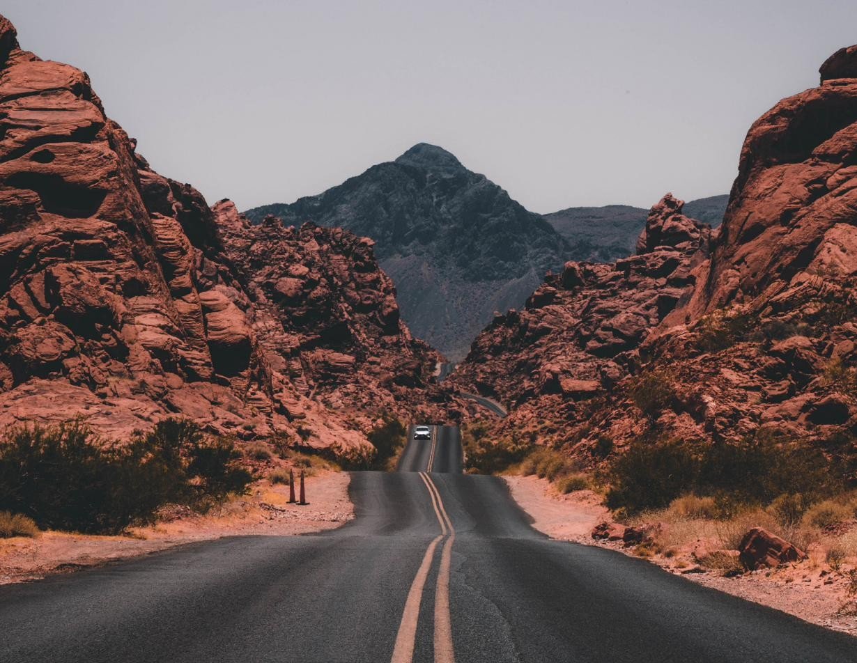 A road running through a narrow pass between rock formations toward a distant peak.
